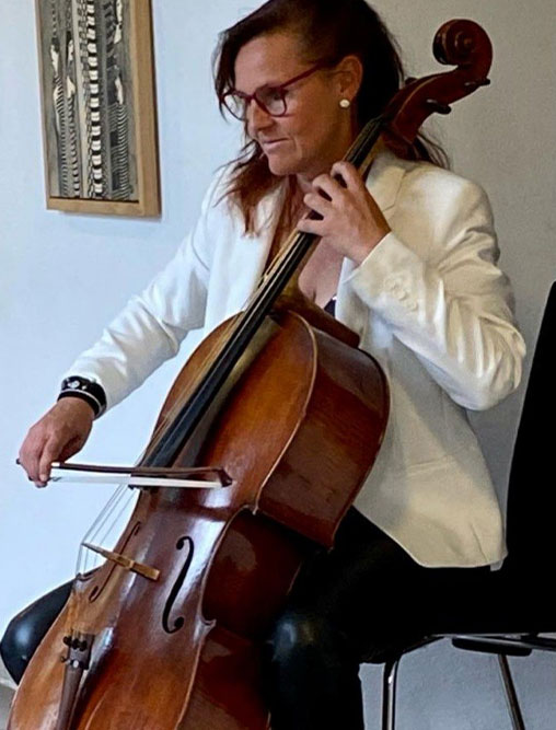 Cellistin spielt Violoncello in weißem Blazer vor einem Kunstwerk