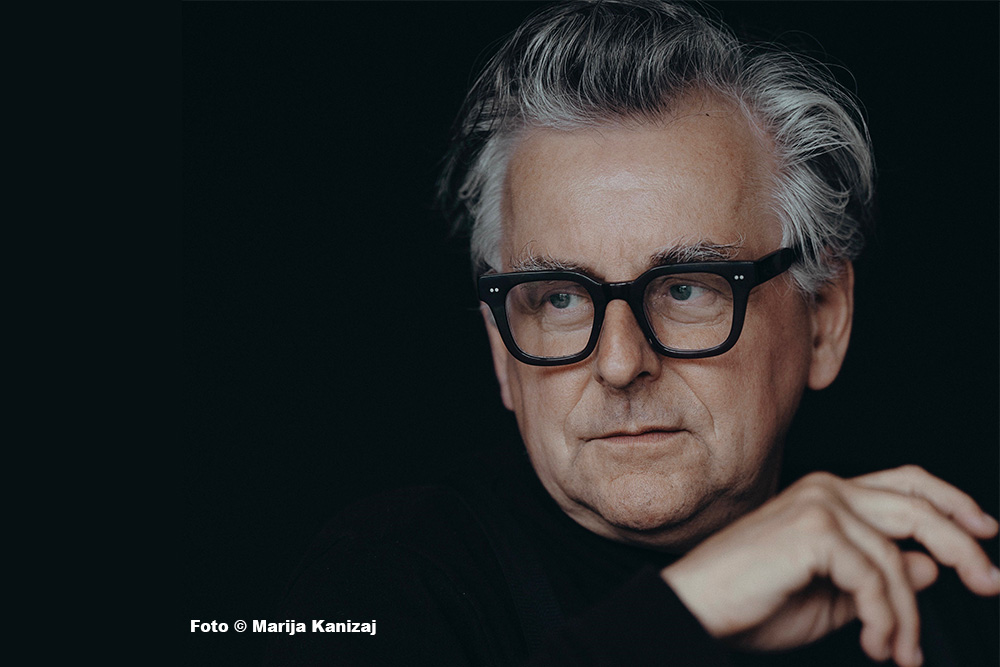 Mann mit Brille und grauem Haar vor schwarzem Hintergrund